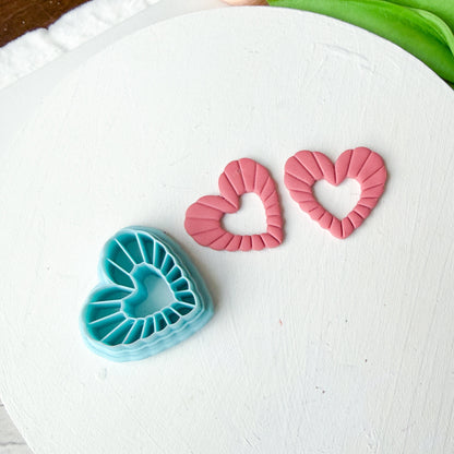 Heart-shaped cookie cutters on a white surface with green fondant and pink fondant.