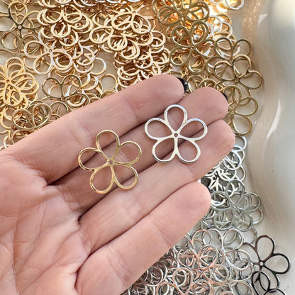 Hand holding a silver flower-shaped earring with a white dish filled with various metal flower-shaped jewelry pieces.