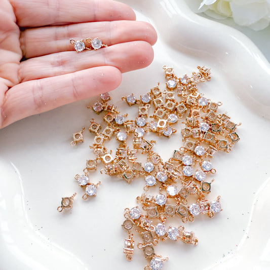 Gold and crystal earring components on a white surface with a hand holding a completed earring.